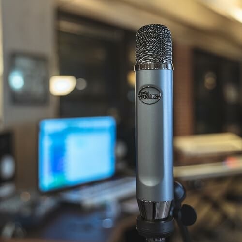 Microphone in a recording studio with blurred computer screen.